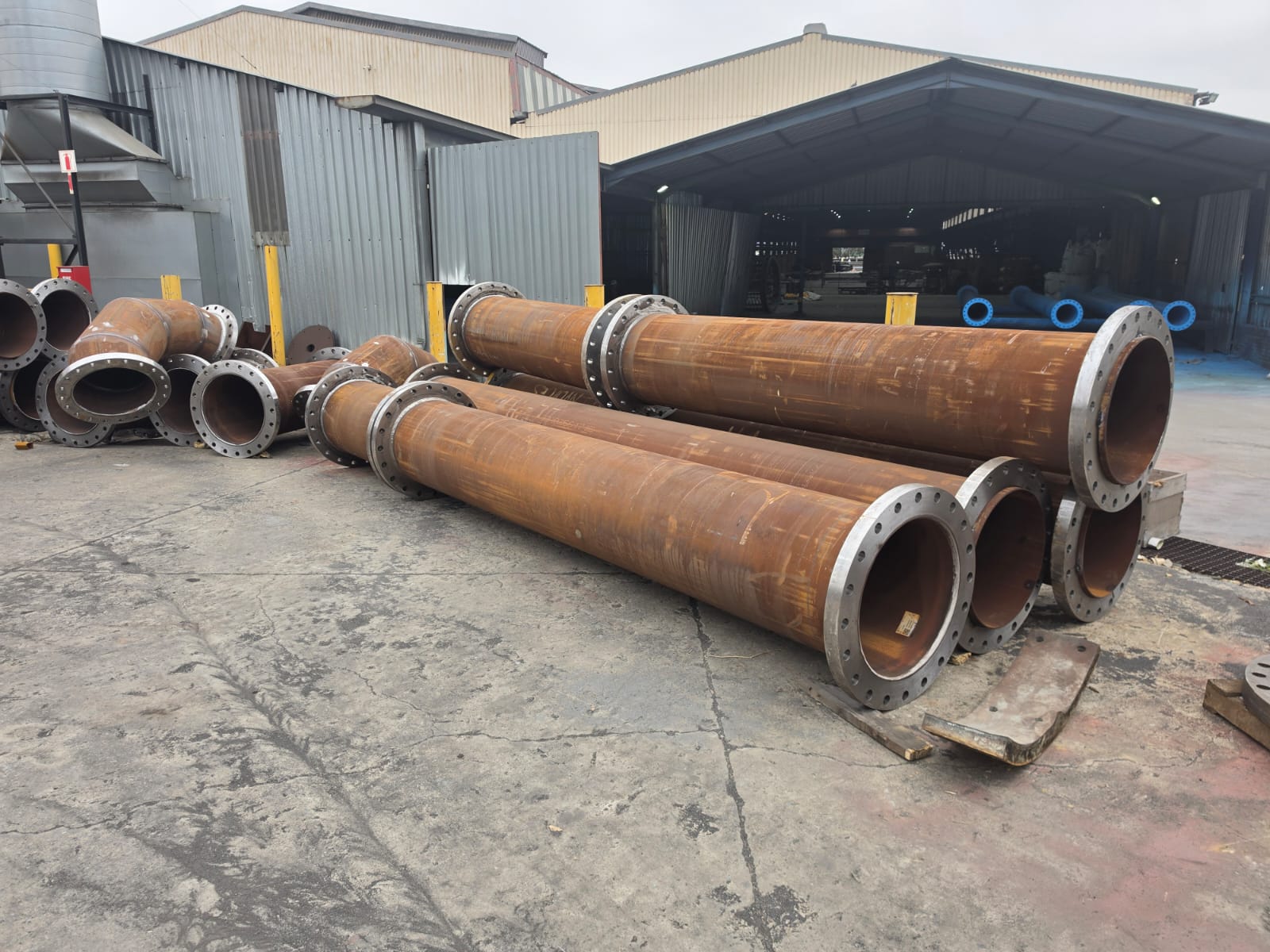 Flanged carbon steel pipe spools and elbows staged outside the Wetpipe fabrication workshop
